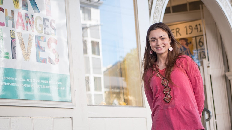 A students stands in front of a building that says art changes lives.