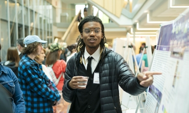 Student presenting research, pointing to a poster at the Steinmetz Research Symposium Poster Day.