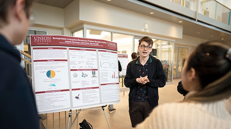 A student presents his research in front of a poster during the annual Steinmetz Research Symposium at Union College